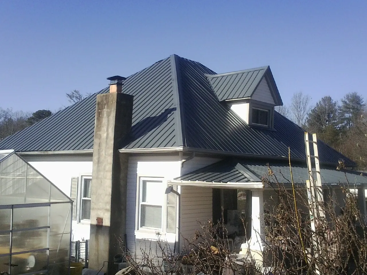 Dark blue standing seam metal roof on a white farmhouse with dormer — Slate & Tile Roof Repair by Roofing Brothers in Shenandoah