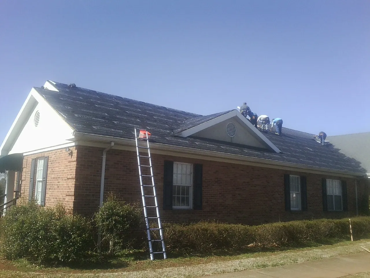 Crew tearing shingles off a brick ranch roof with a ladder set — Emergency Roof Repair work by our crew in Shenandoah