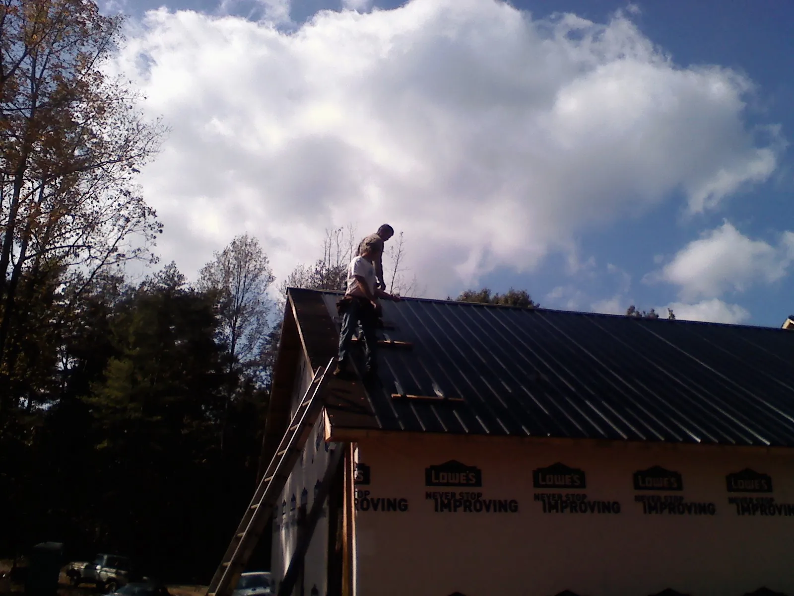 Roofer fastening dark metal panels high against a cloudy sky, from a Roof Inspection job in Shenandoah