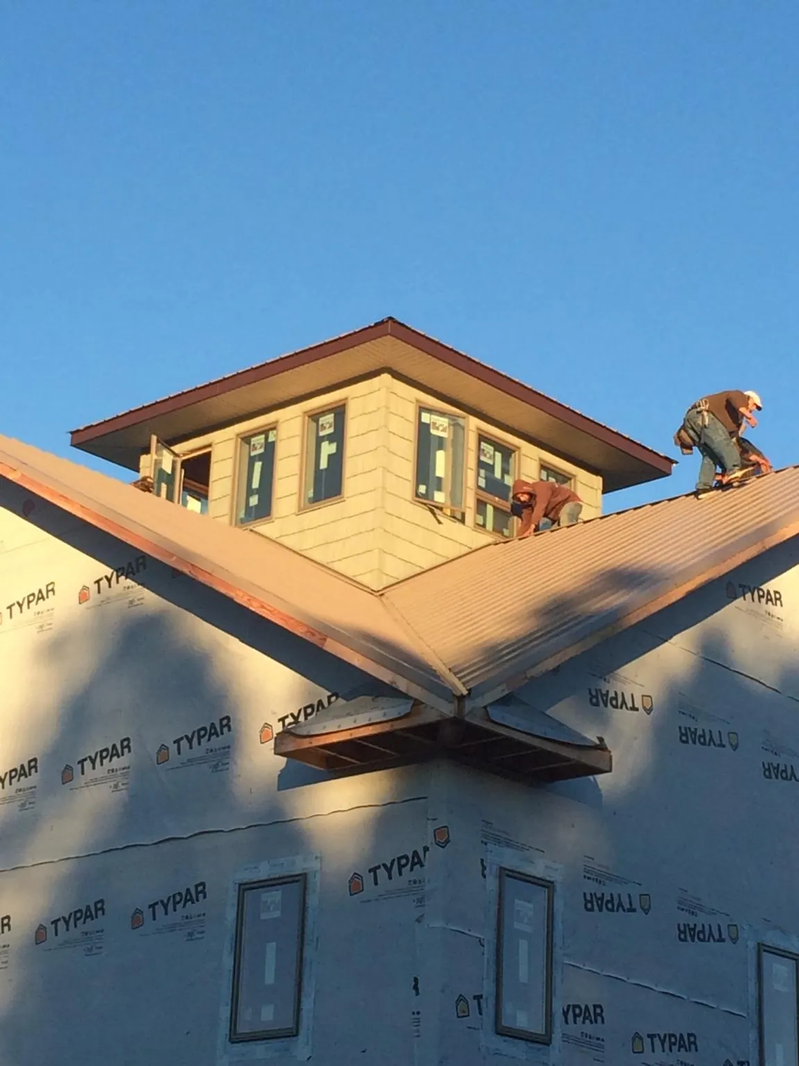Roofers working around a rooftop cupola on a new metal roof at sunset — Roof Waterproofing in Shenandoah by Roofing Brothers